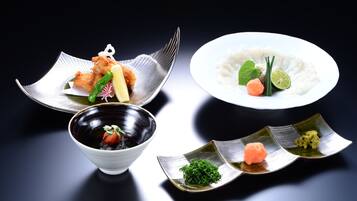 A variety of Japanese dishes including tempura, rice with fish, and sashimi on a dark background.