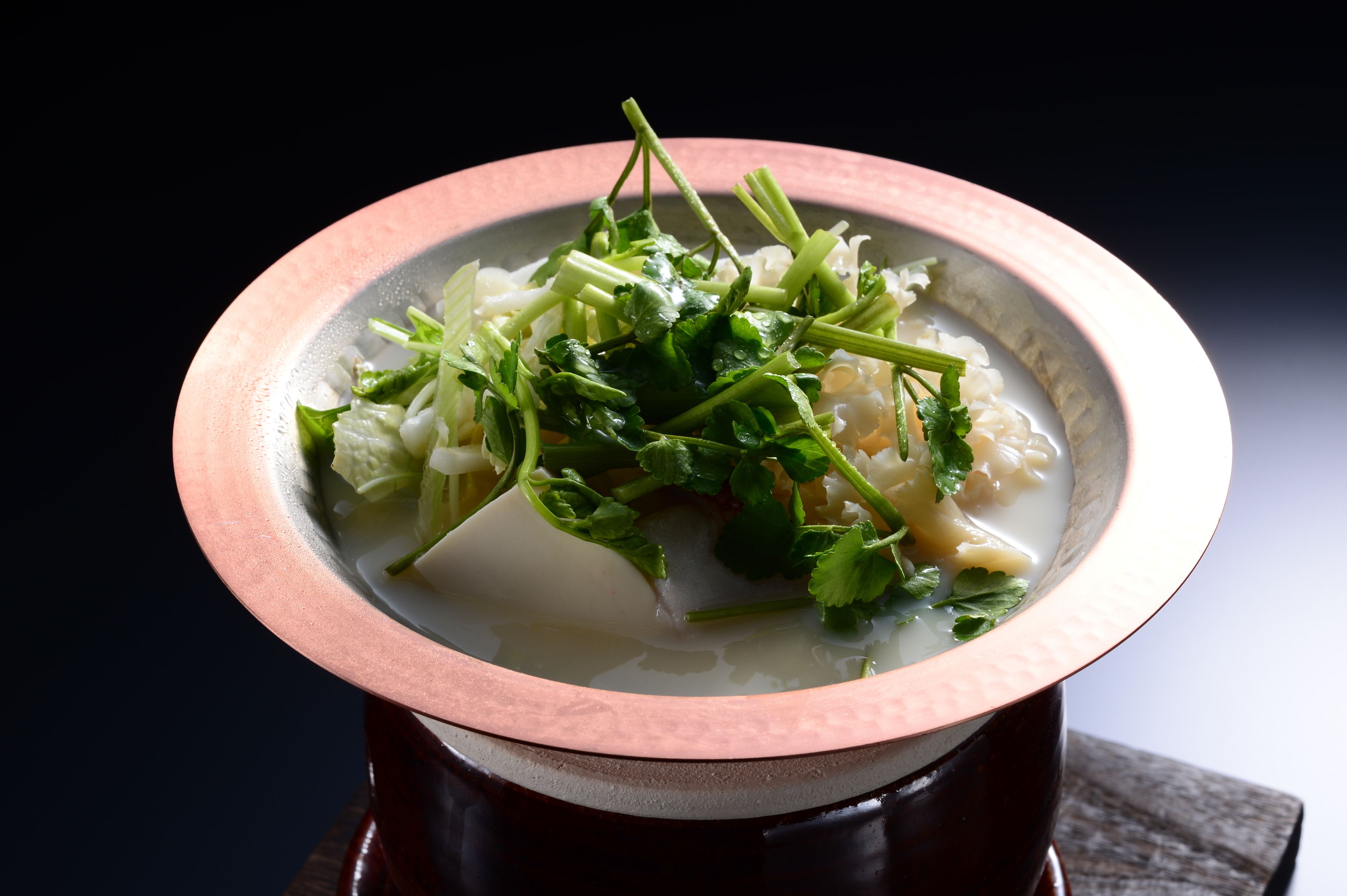 Un bol de soupe contenant des légumes verts et des herbes, posé sur une surface sombre.