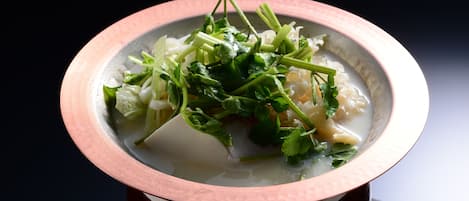 A bowl of soup with green vegetables and herbs on a dark surface.