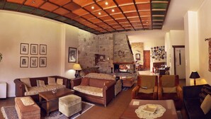 A cozy living room with a stone fireplace, wooden ceiling, and a variety of seating options including sofas and armchairs.