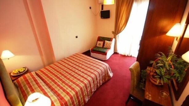 Una habitación de hotel pequeña y acogedora con una cama individual, una silla, un escritorio con lámpara y una planta en maceta.
