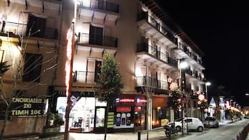 A multi-story building with balconies, a storefront with a sign, and a tree in front.