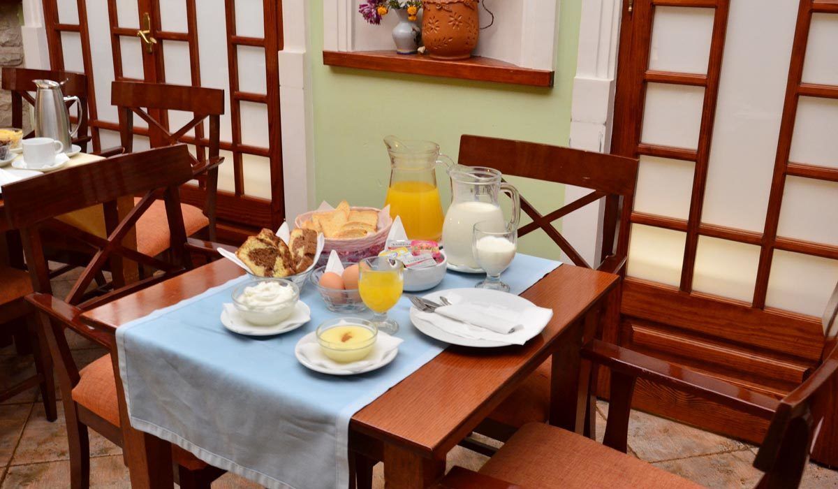 Une table de petit-déjeuner dressée avec divers aliments, une carafe de jus d’orange et un pot à lait.