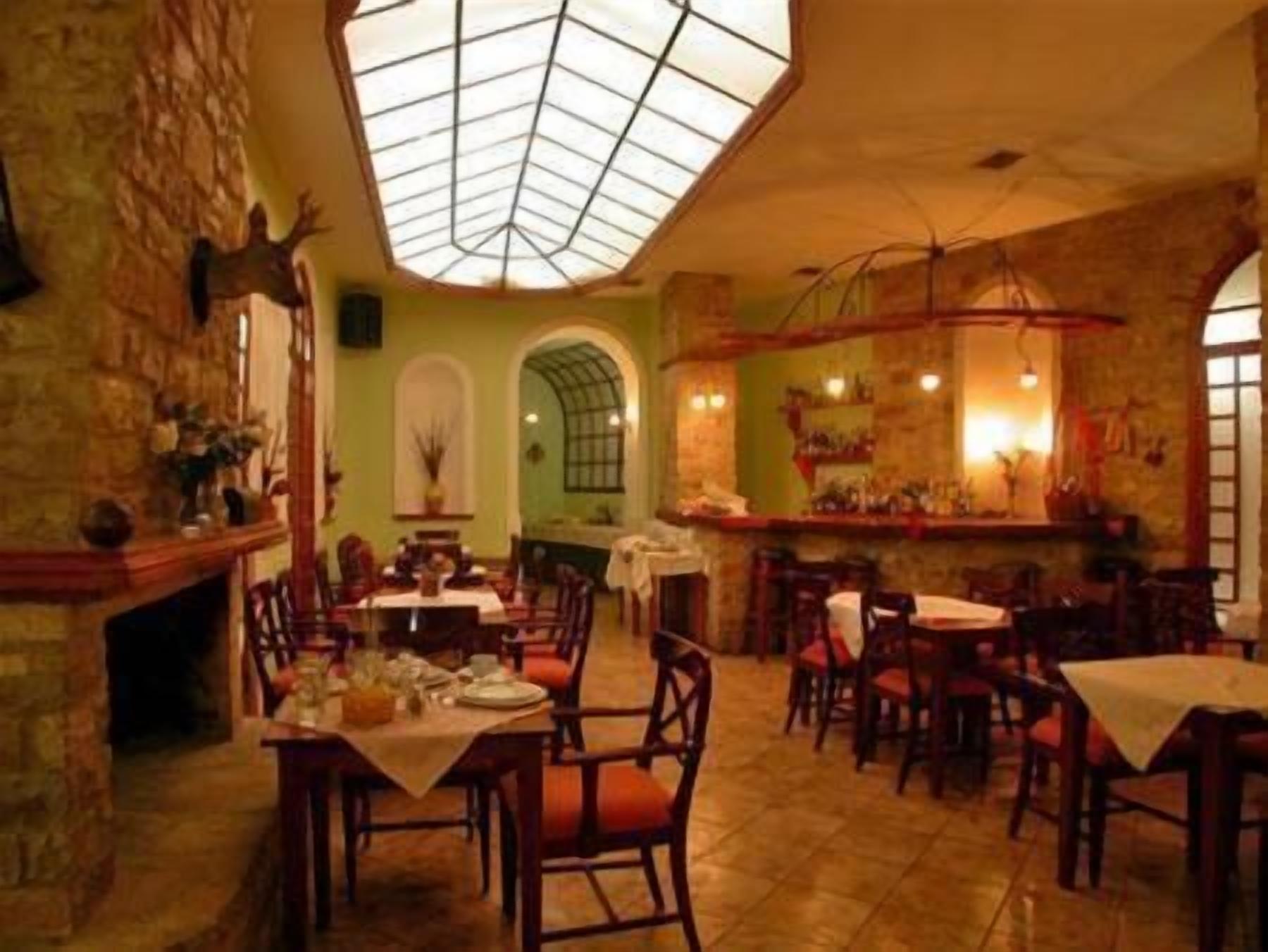 A restaurant with a high ceiling and a skylight, featuring wooden tables and chairs, stone walls, and a brick floor.
