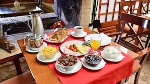A breakfast table set with various food items and a coffee pot, with a fireplace in the background.