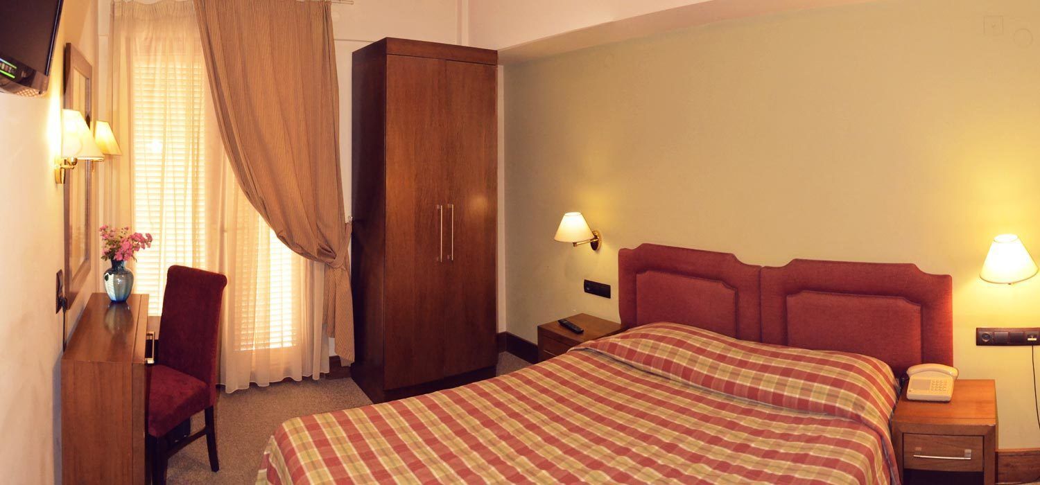 A hotel room with a bed, a wardrobe, a desk with a chair, and bedside lamps.