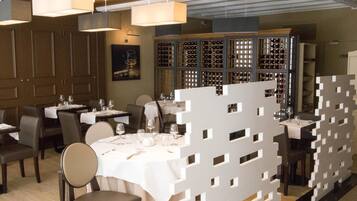 A restaurant with tables set for dining, a wine rack in the background, and a decorative partition in the foreground.