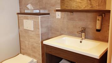 Een moderne badkamer met een wit wastafelmeubel, een spiegel erboven en een toilet aan de linkerzijde.