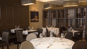 Un restaurante con mesas redondas dispuestas para comer, estanterías llenas de vino al fondo y una obra de arte enmarcada en la pared.
