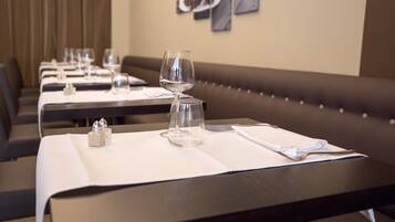 Un restaurante con mesas dispuestas para comer, cada una con una copa de vino y cubiertos.