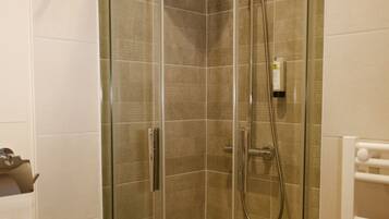 A glass-enclosed shower stall with a handheld showerhead and a handheld faucet.