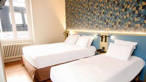 Habitación de hotel con dos camas individuales, un papel tapiz estampado y ventana con vistas.