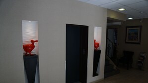 Un pasillo con dos esculturas rojas sobre pedestales, una escalera y un cuadro enmarcado en la pared.