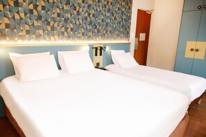 A hotel room with two beds, a geometric patterned wall, and a wooden wardrobe. - Hôtel de France Vire (Vire-Normandie)