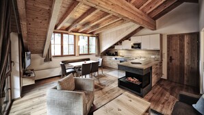A spacious loft with a high ceiling, wooden beams, a dining area with a table and chairs, a kitchen with modern appliances, and a fireplace. - Hotel & Luxury Appartements Dorfstadl (Kappl)