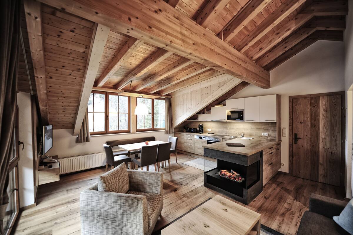 Un loft espacioso con techo alto, vigas de madera, una zona de comedor con mesa y sillas, una cocina con electrodomésticos modernos y una chimenea.