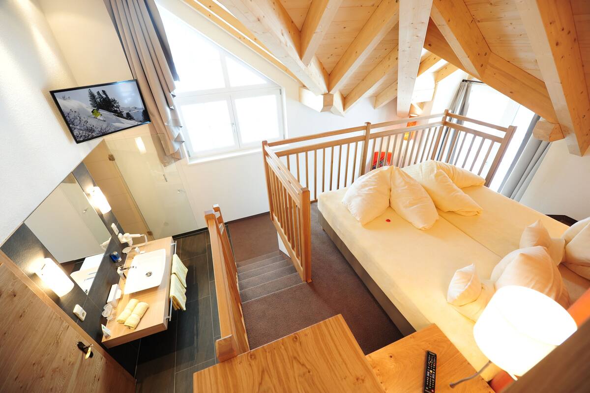Un dormitorio con una cama litera de madera, un escritorio pequeño con una silla, un espejo y una ventana con cortinas.