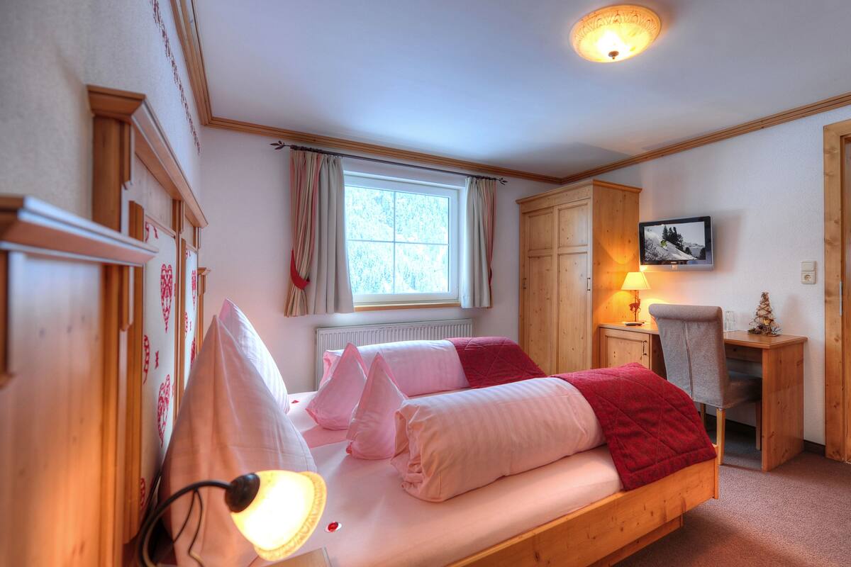 Un dormitorio con una cama de madera, un escritorio, una silla, un radiador y una ventana con cortinas.