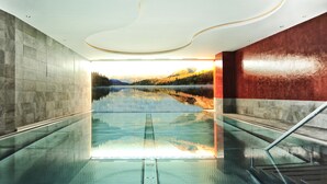 A modern indoor pool with a glass floor, surrounded by stone walls and a view of a lake and mountains. - Hotel & Luxury Appartements Dorfstadl (Kappl)