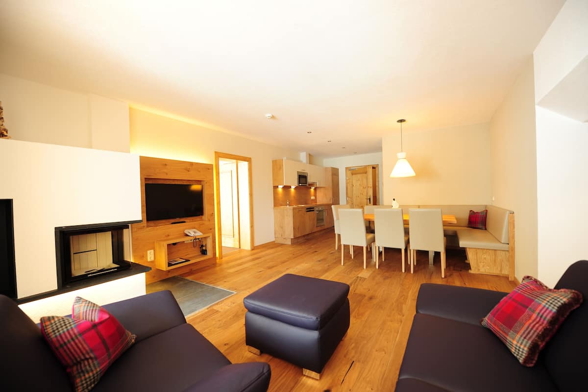 Una sala de estar moderna con chimenea, un comedor con mesa y sillas, y una cocina al fondo.