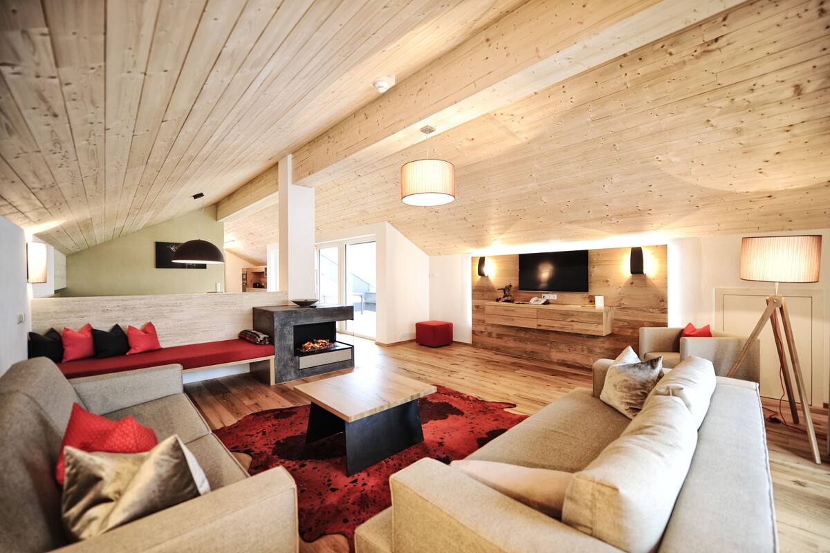 Una sala de estar moderna con techo de madera, chimenea, televisor y una alfombra roja.