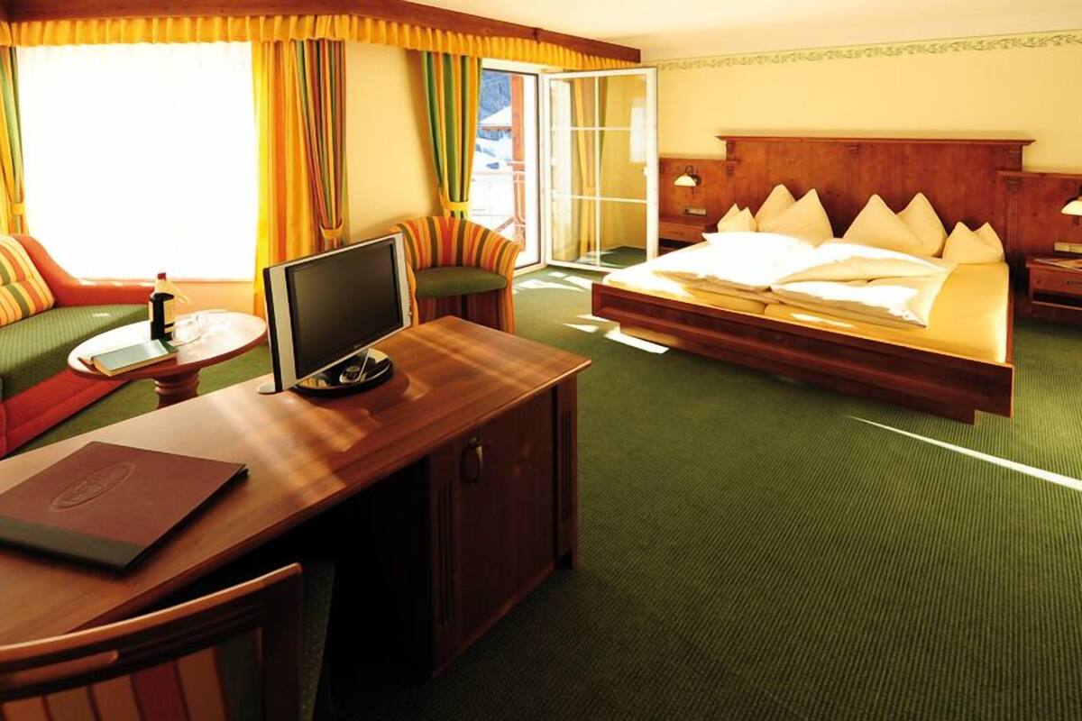 Habitación de hotel con una cama, un escritorio con computadora, una silla, un sofá y una ventana con cortinas.
