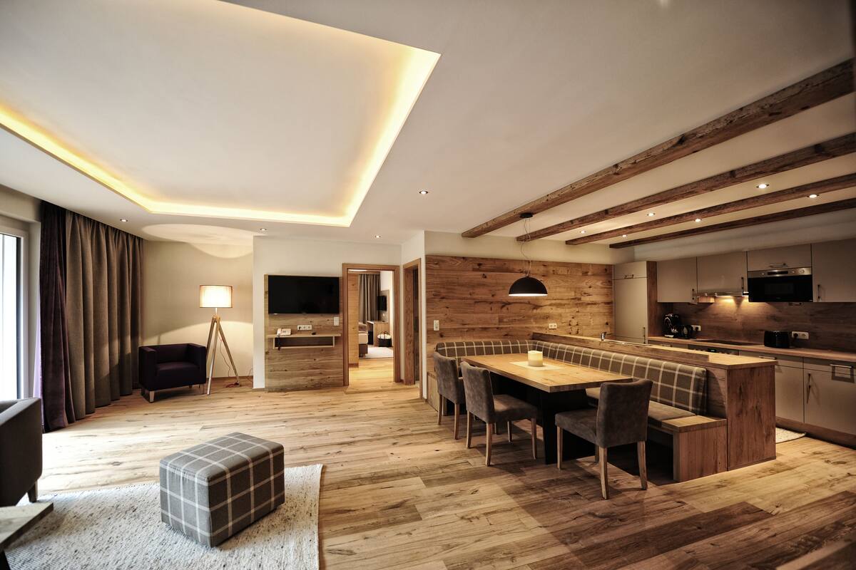 Una cocina moderna con vigas de madera, un comedor con banco y un televisor al fondo.