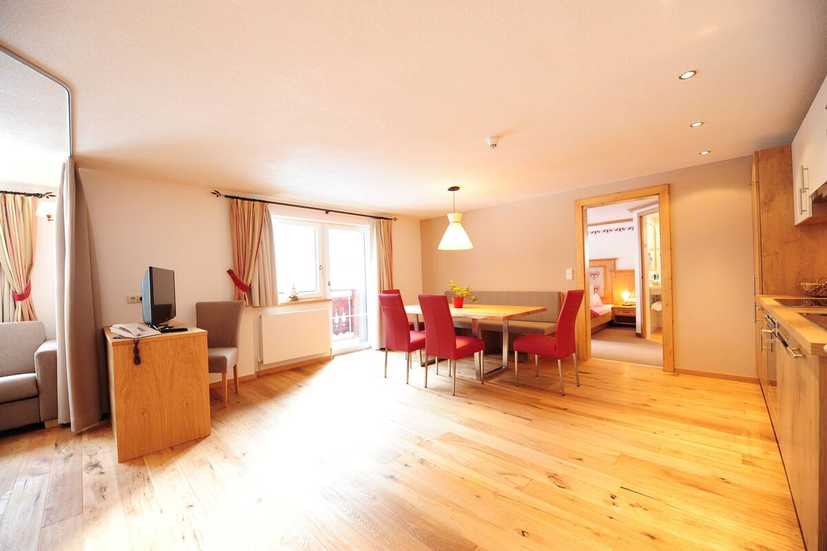 Una sala de estar moderna con piso de madera, un sofá, un televisor y un comedor con sillas rojas.