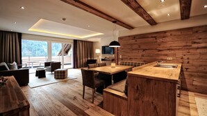 A modern kitchen with wooden accents, a dining area with a large table and chairs, and a view of a mountainous landscape through the windows. - Hotel & Luxury Appartements Dorfstadl (Kappl)