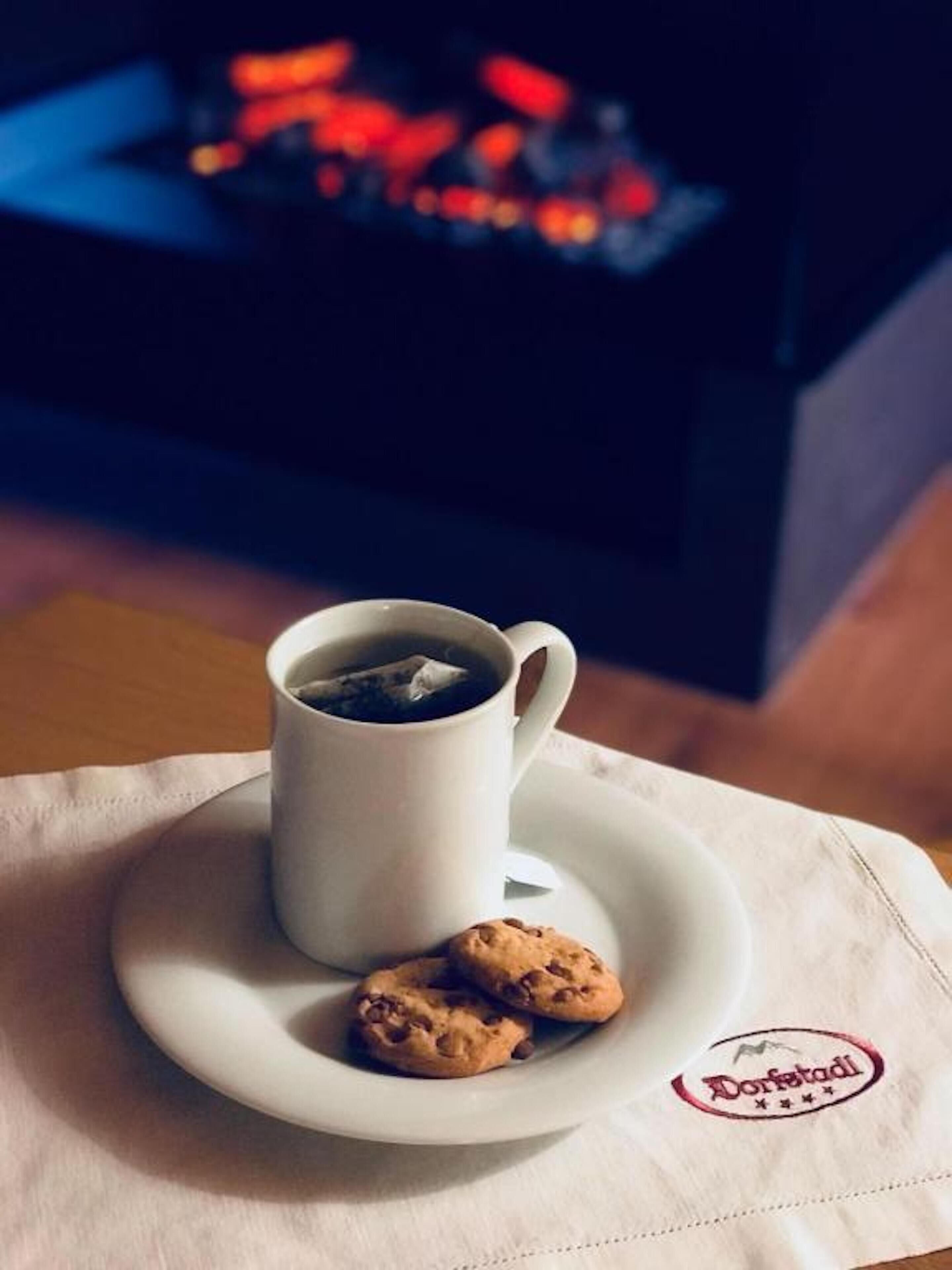 Una taza de café con una galleta sobre un platillo, colocada sobre una mesa con un mantel que tiene un logotipo.