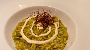 En tallrik med grön risotto, vit sås och saffransdekoration, placerad på ett bord med ljus och vinglas.