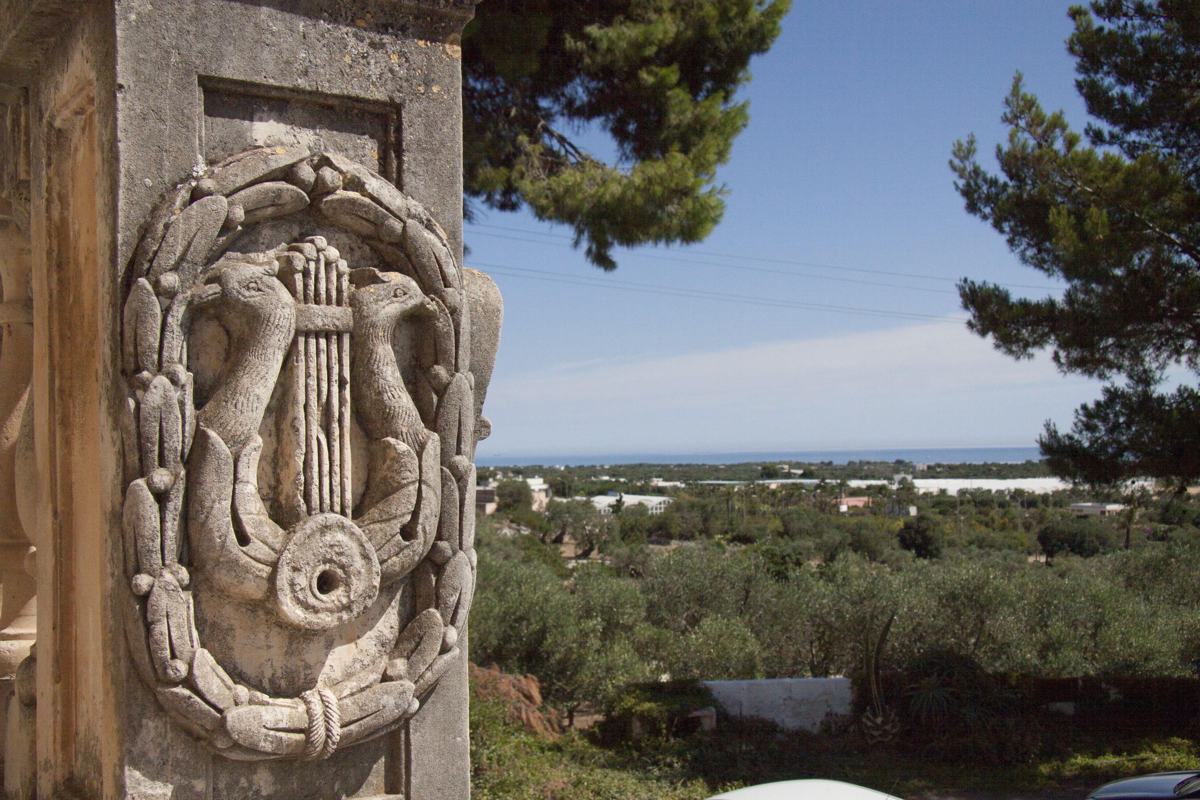 Un relieve pétreo en la fachada de un edificio, con vistas a un paisaje con árboles y edificios lejanos.