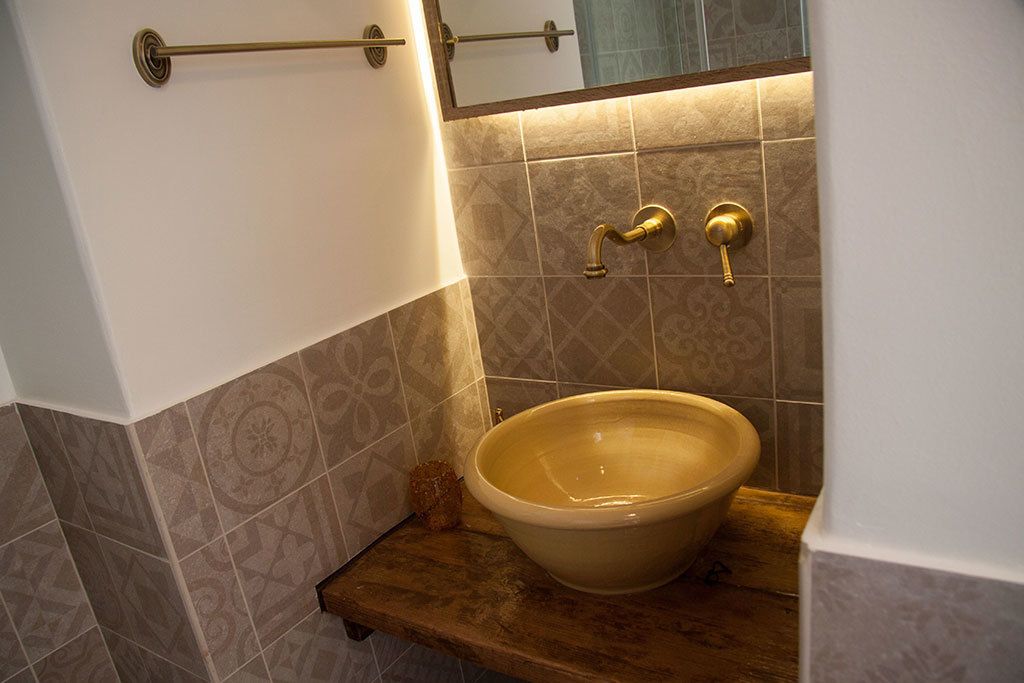 A bathroom with a beige sink, a wooden shelf, and patterned tiles.