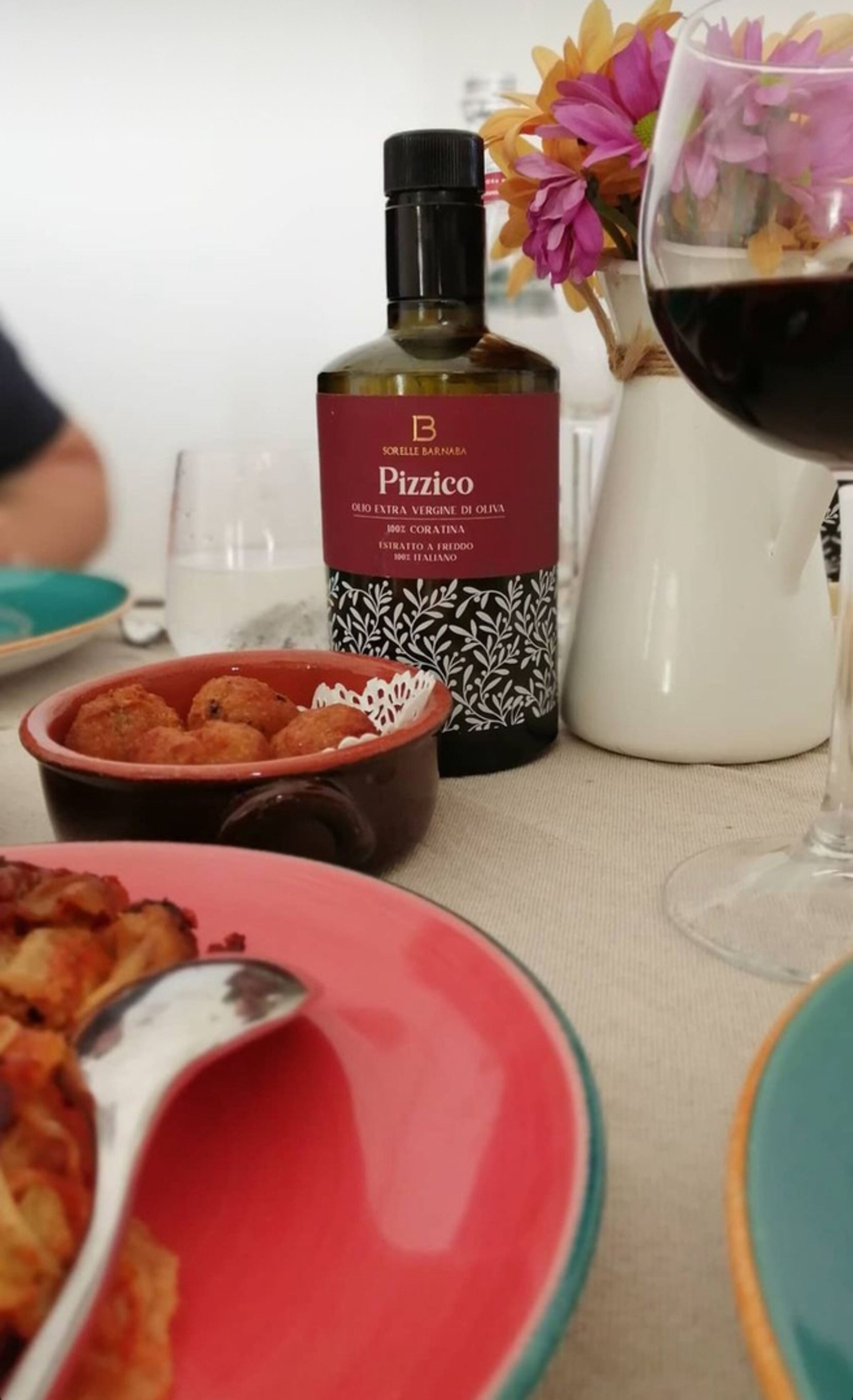 A table with a bottle of Pizzico, a glass of red wine, and a bowl of food.