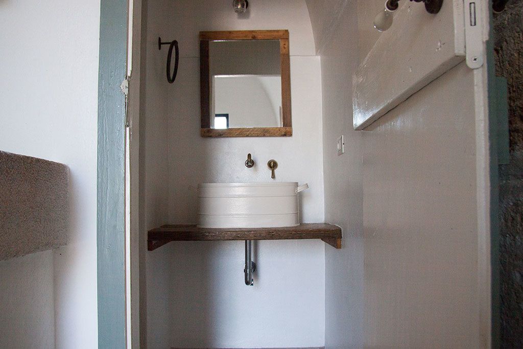 Un bagno con un lavandino bianco, uno scaffale di legno e uno specchio sopra.