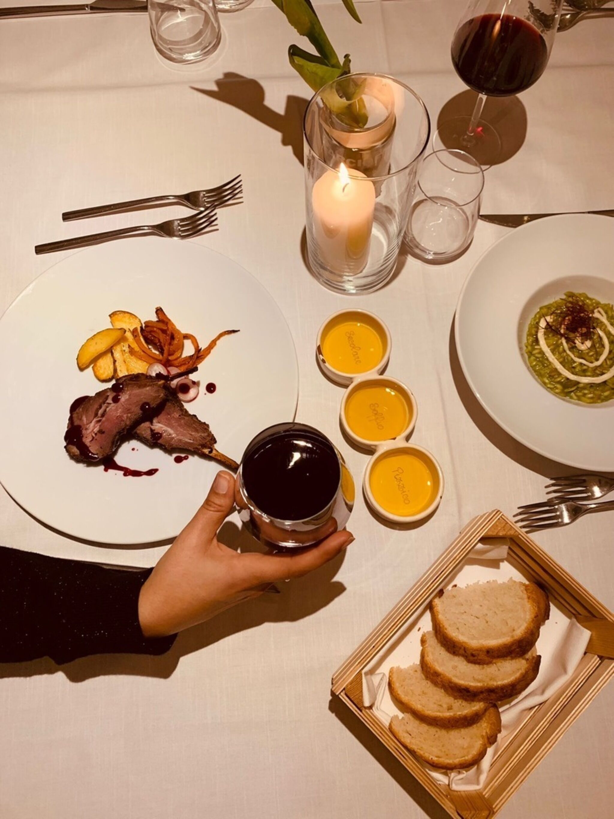 A dining table with plates of food, a candle, and a glass of red wine.