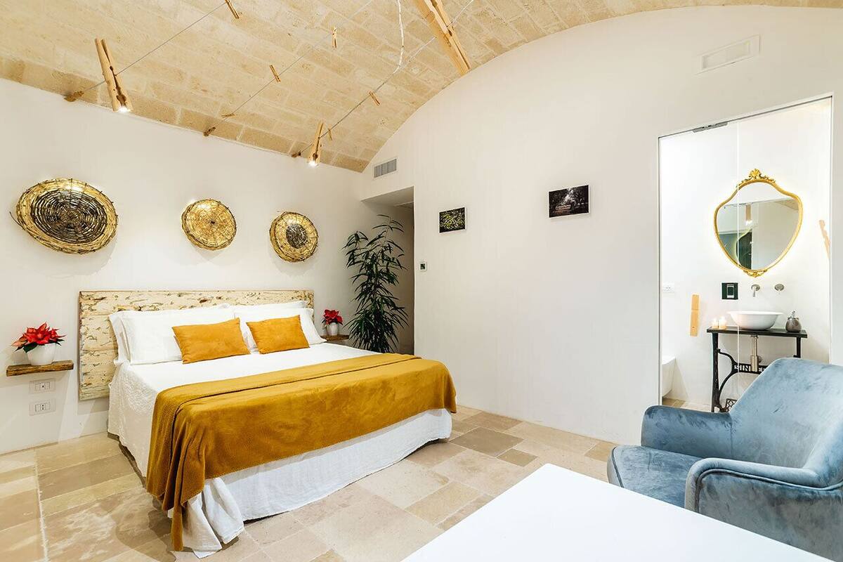 Une chambre à coucher avec un lit, une chaise bleue, un miroir et des œuvres d’art décoratives au mur.