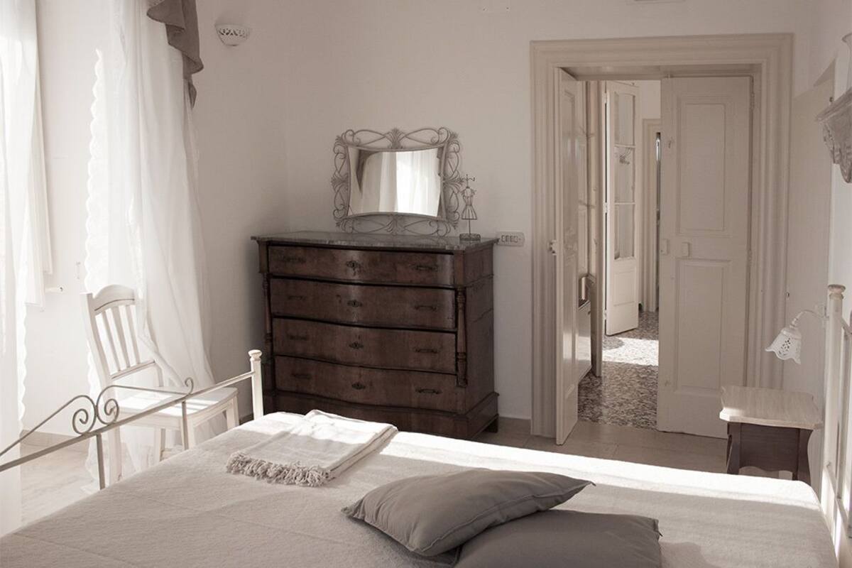 Une chambre à coucher comprenant un lit, une commode, un miroir et une porte donnant sur une autre pièce.