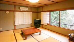 A traditional Japanese room with tatami flooring, a wooden table, a television, and a window with a view of trees.