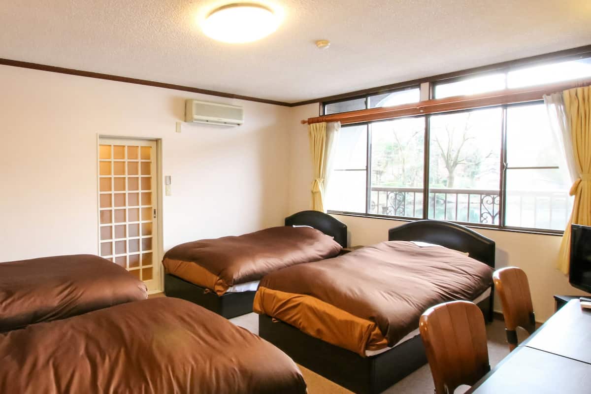 Habitación de hotel con dos camas, un escritorio, una silla, una ventana con cortinas y una puerta corrediza.