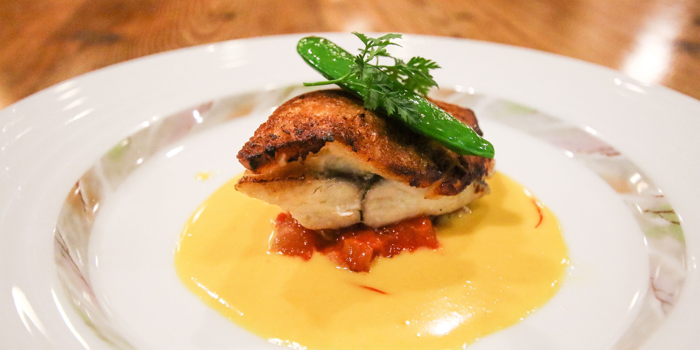 A plate with a piece of grilled chicken, a green garnish, and a yellow sauce.