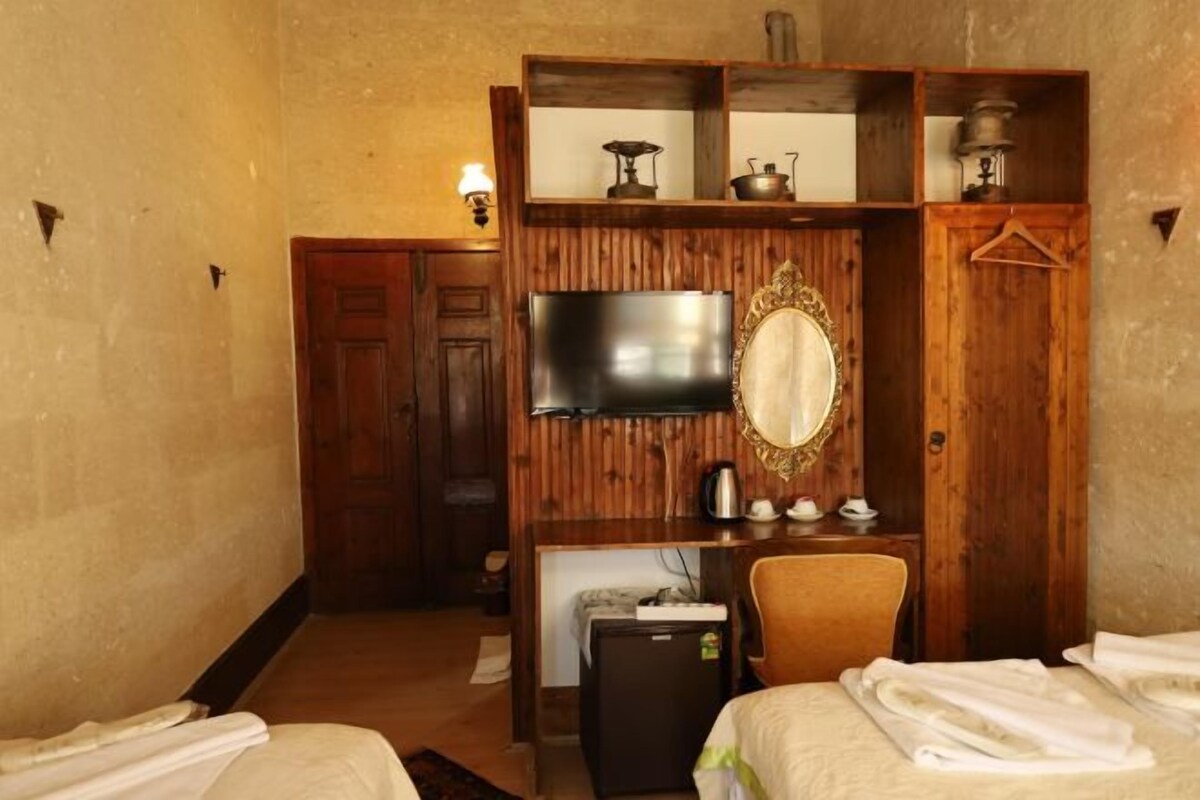 Una camera d'albergo con un armadio in legno, una televisione, uno specchio, una scrivania con un bollitore e due letti.