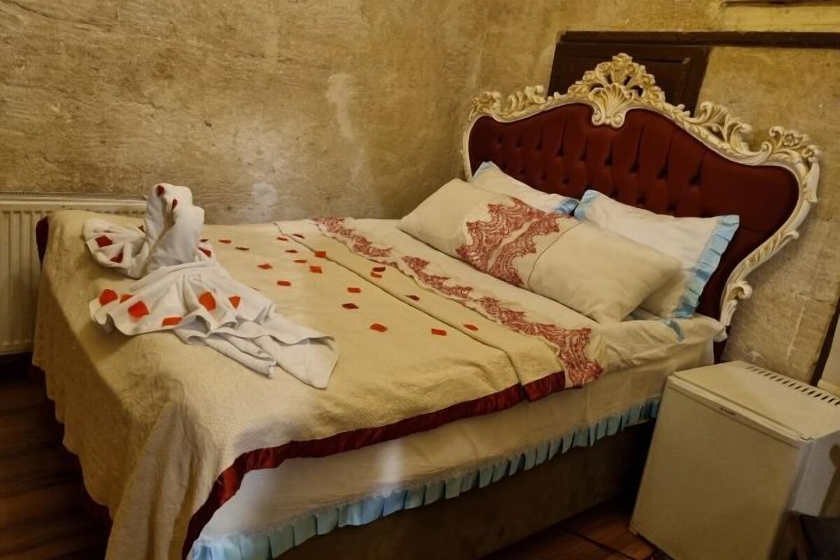A bed with a red headboard, a white blanket, and a white towel on the bed.