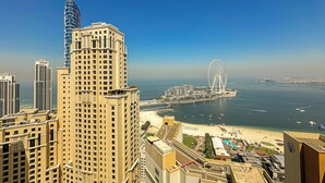 Um edifício alto com design moderno, vista para a orla marítima e uma roda-gigante ao longe.