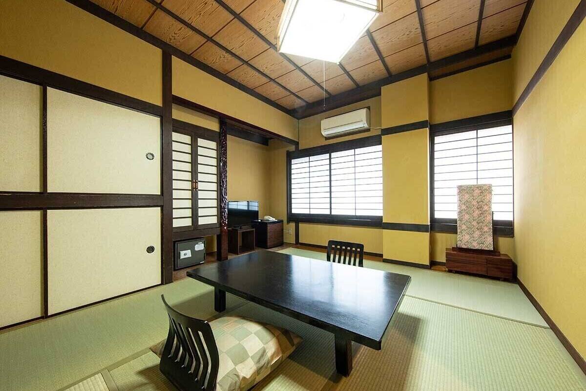 A tatami mat room with a low table, chairs, a television, and sliding doors.