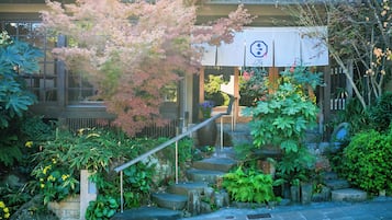 A traditional Japanese building with a stone staircase, surrounded by lush greenery and flowering plants.