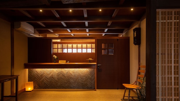 Un área de recepción con un mostrador de madera, una planta en maceta y una puerta con panel de vidrio.