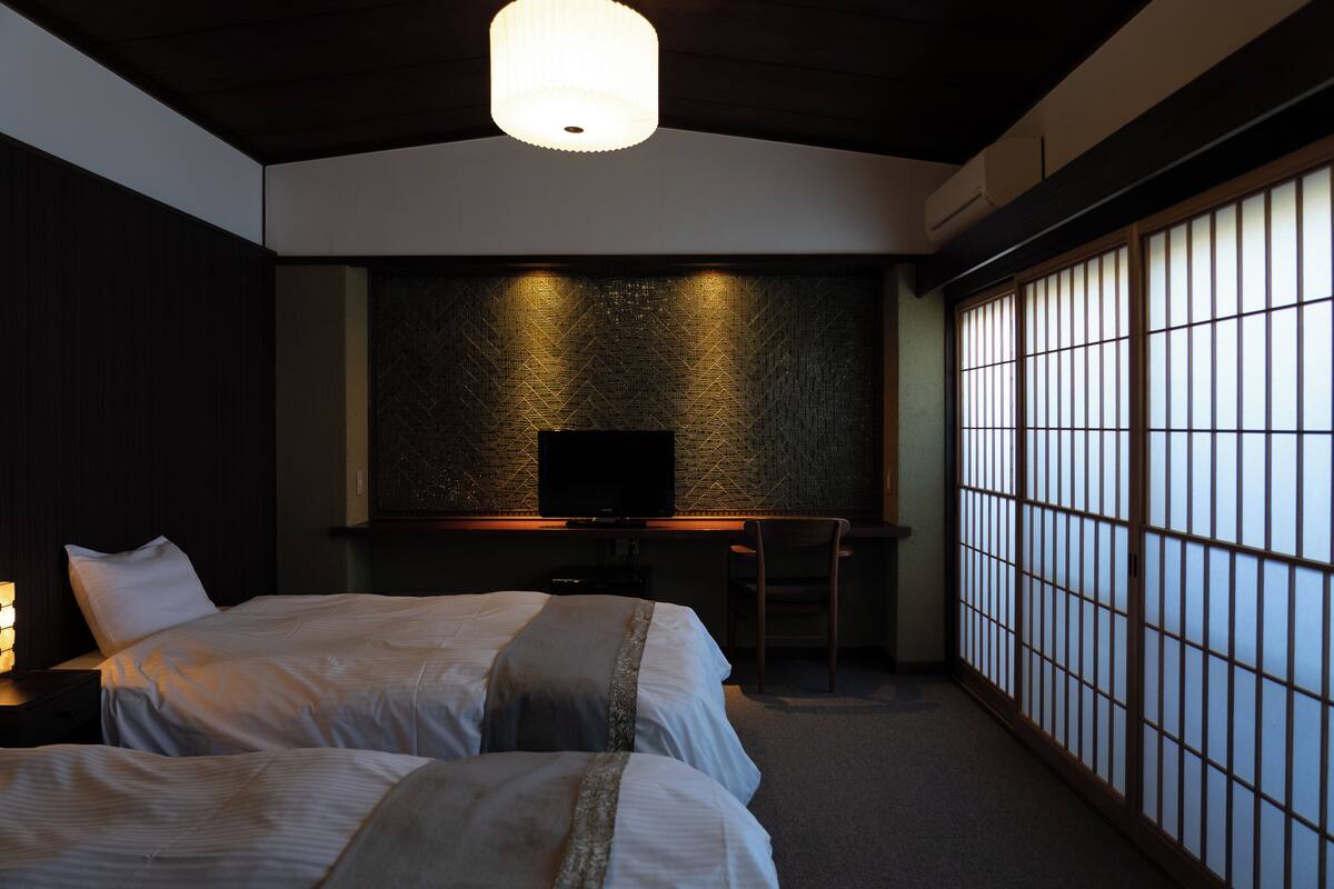 A hotel room with two beds, a desk, a chair, and a television.