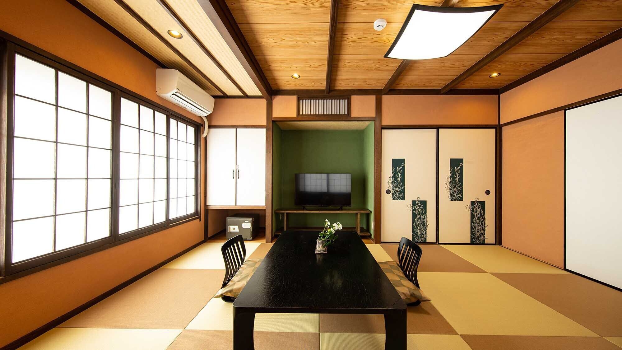 A traditional Japanese-style room with tatami flooring, a tatami mat table, a television, sliding doors, and a ceiling light fixture.