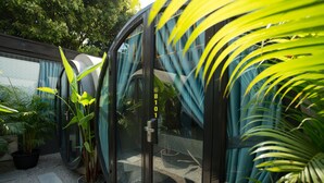 A modern glass door with a visible door number, surrounded by potted plants and a gravel path. - White Rabbit Hostel - Adults Only (Siem Reap)